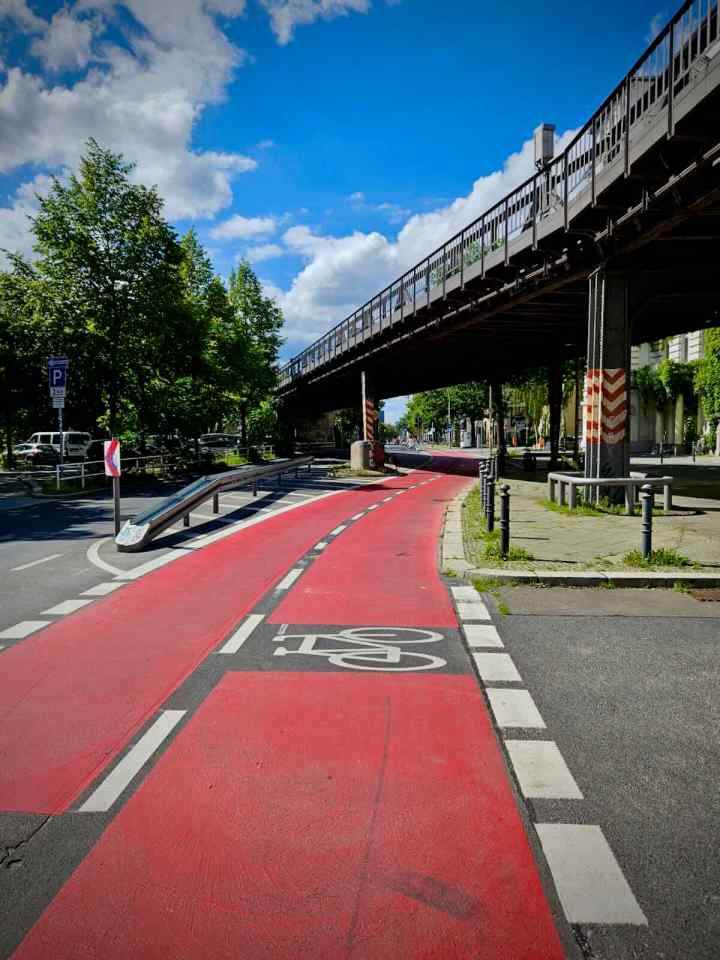 Red painted cycle lane passing under U-Bahn viaduct on Bülowstraße