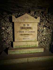 Skulls and bones, with a gravestone in the Paris Catacombs
